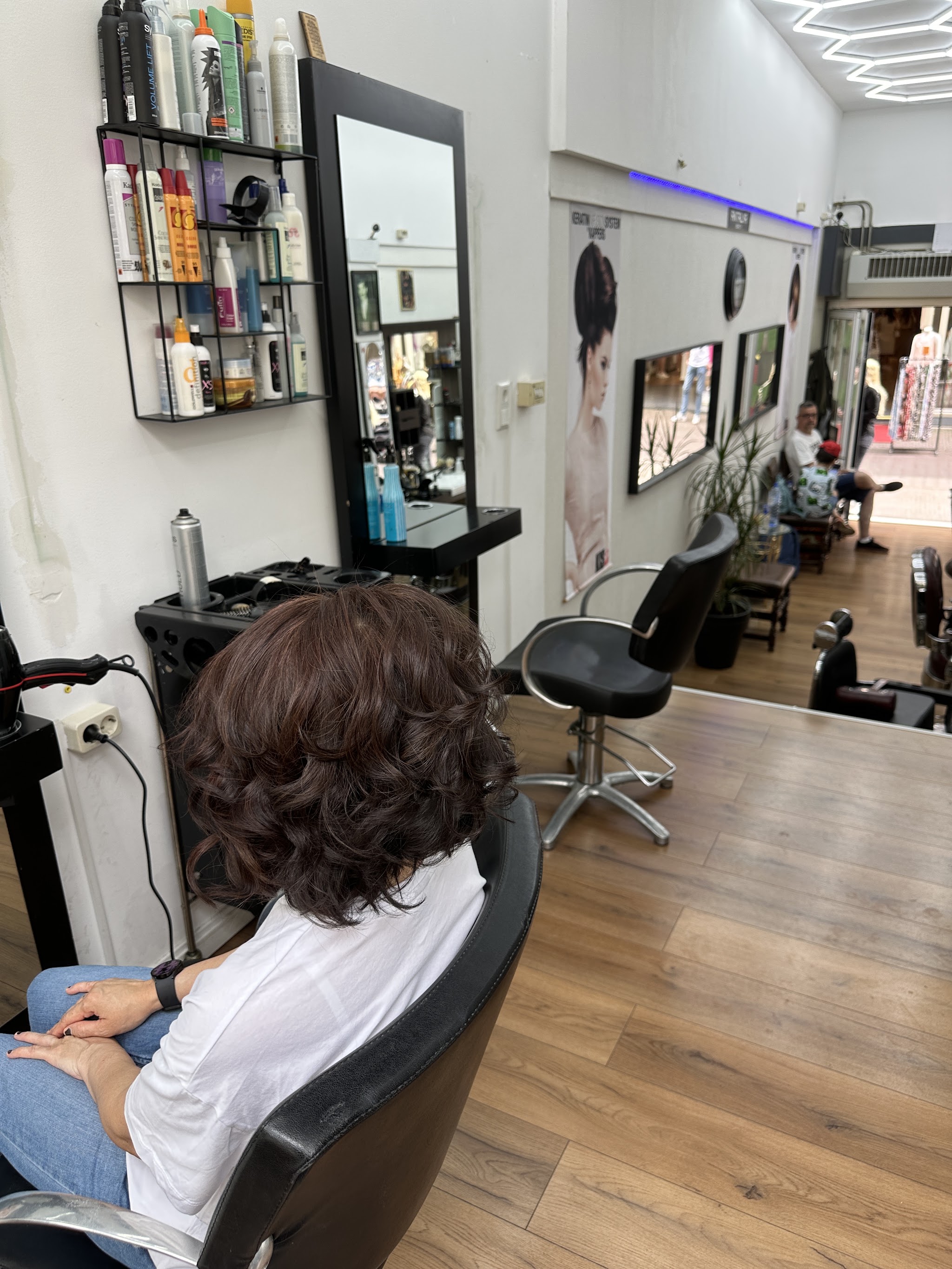 Klant met donkere krullen in de stoel, op de houten vloer van de salon