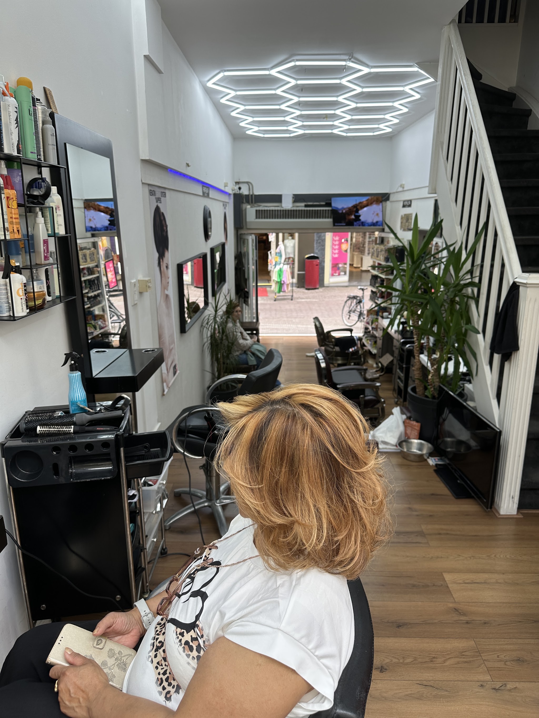 Klant met een blonde bob in de salon, met de trap en de planten op de achtergrond