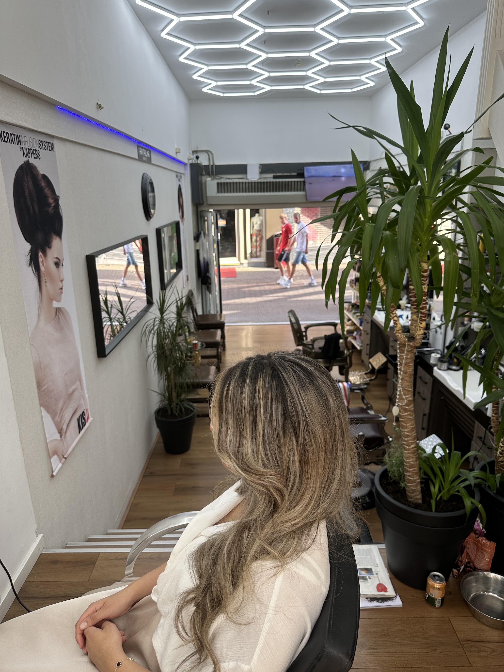 Klant in de stoel met lang haar in laagjes met highlights, in de salon onder de honingraatlampen